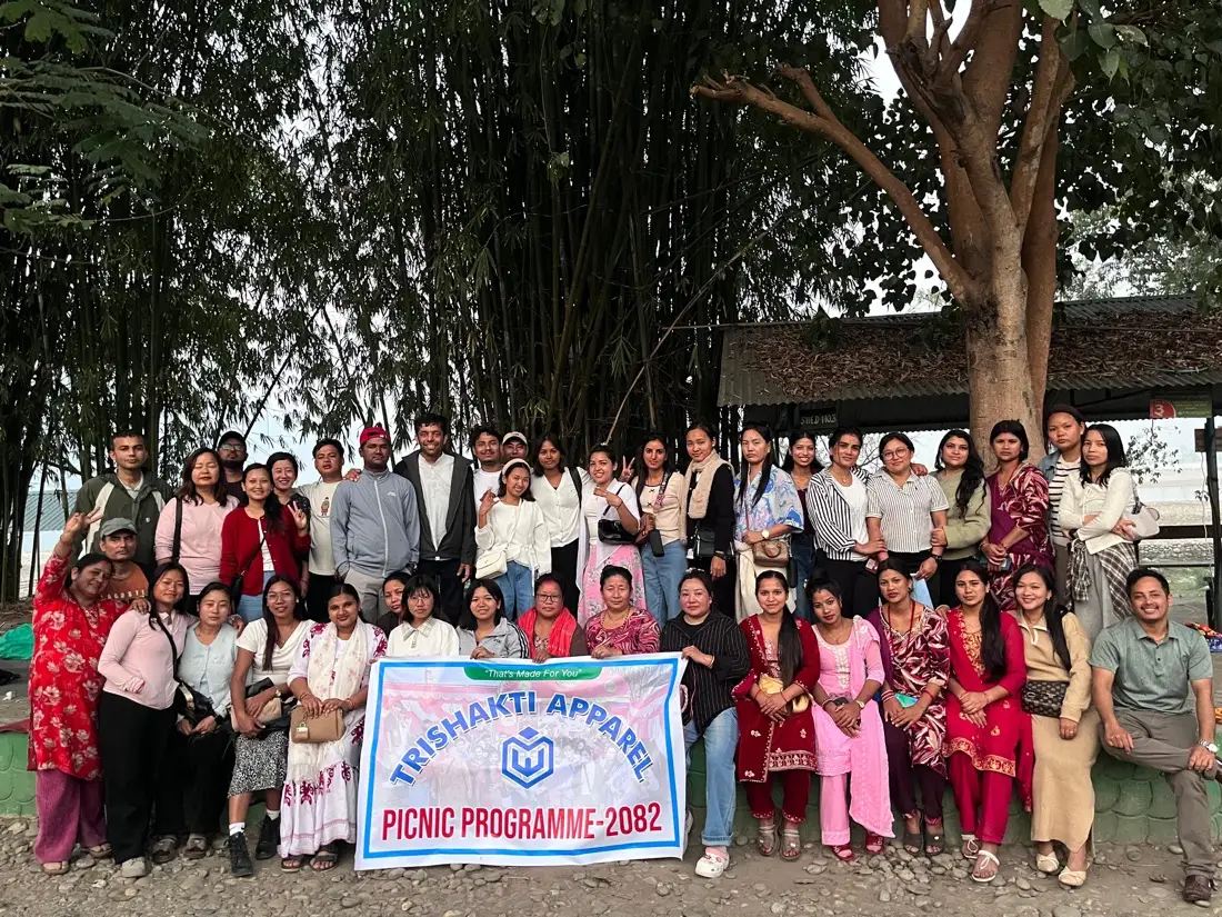 Trishakti Apparel团队在2082年野餐活动（Picnic Programme 2082）上与公司横幅合影