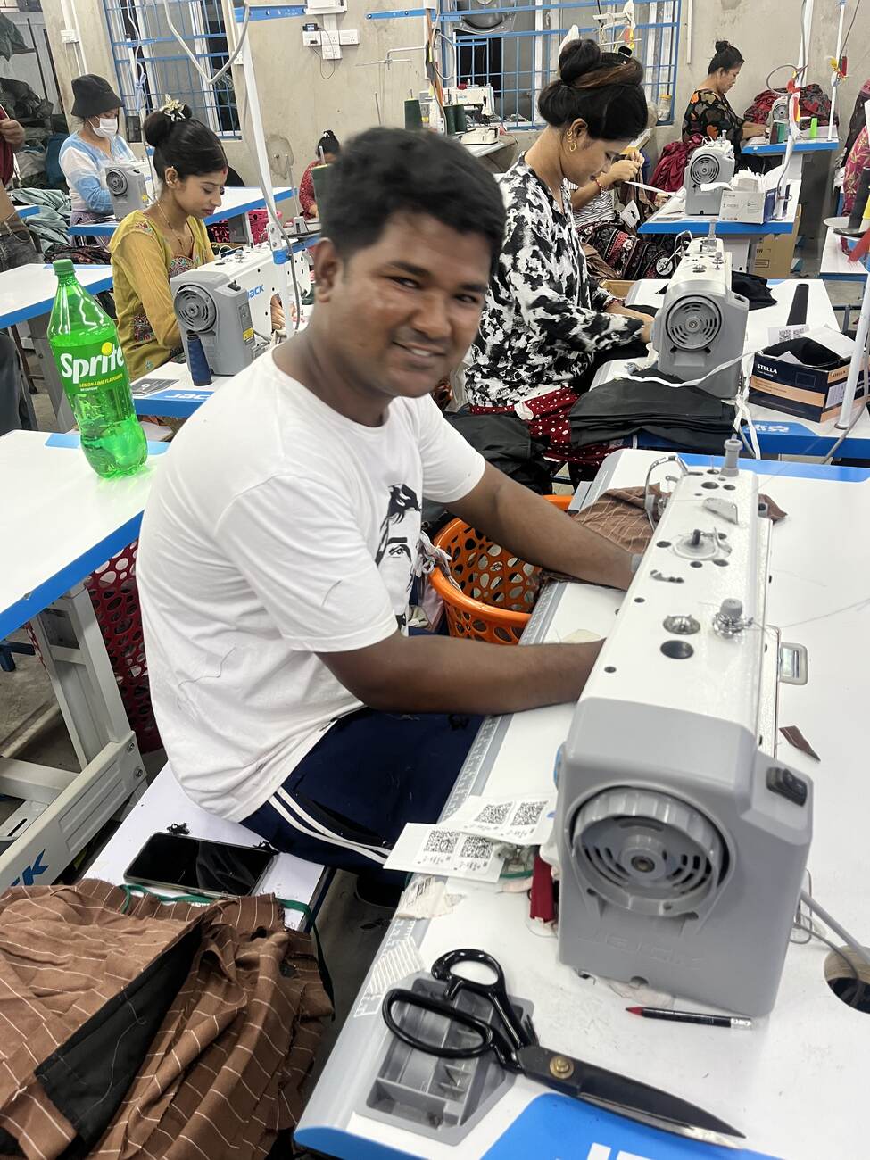 A machine operator sewing at a JACK industrial lockstitch machine on the Trishakti Apparel production floor in Gaindakot, Nepal, with the rest of the sewing line behind